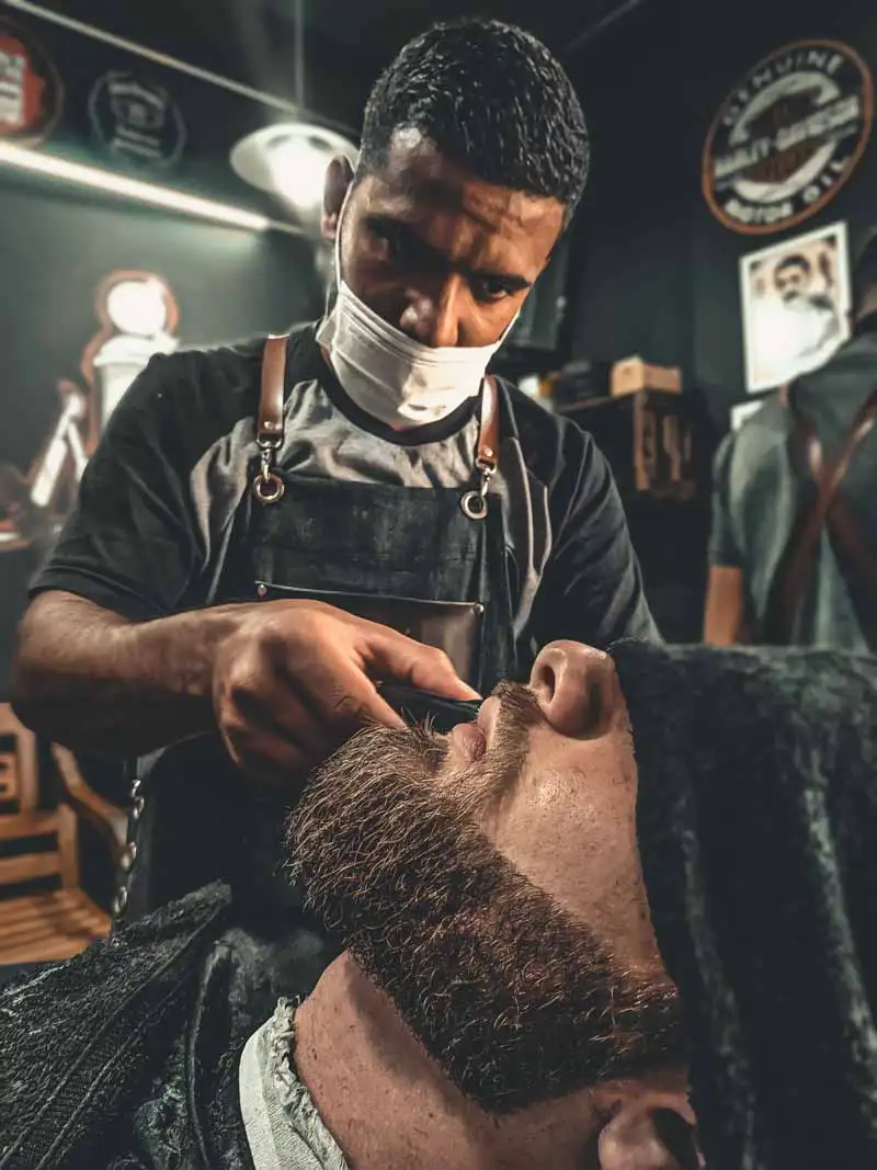 Barber trims a client's thick full beard with a clipper
