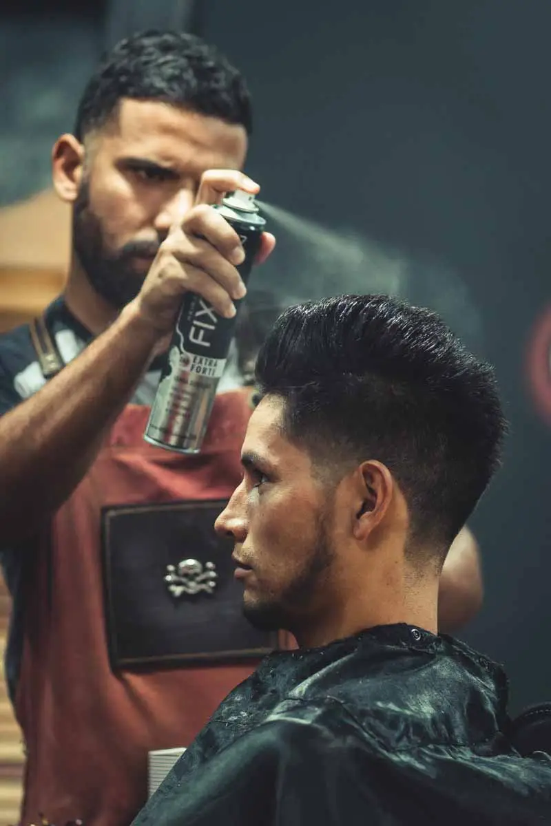 Barber spraying hair styling product on client hair after haircut